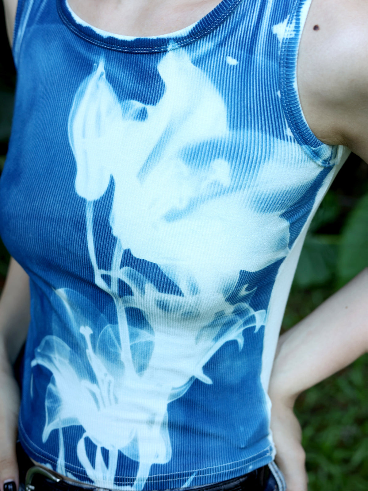 Nahaufnahme des weißen Lilienmotivs auf dem blauen Lily Crop Top, am Model getragen